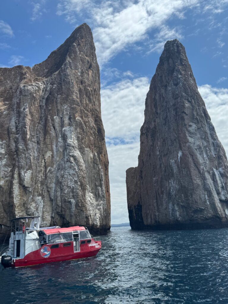 Two multi-story rocks with near-vertical sides thrust out of the ocean. A jaunty red boat is on the water in the foreground